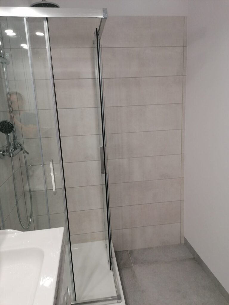 Kabina prysznicowa ze szklanymi drzwiami i jasnymi płytkami, realizacja Remoart