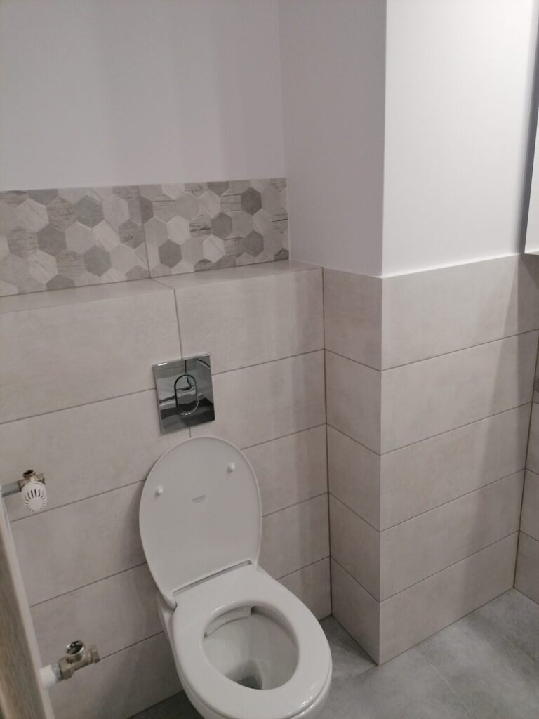 Łazienka z płytkami do połowy ściany i stelażem WC podwieszanego, realizacja Remoart