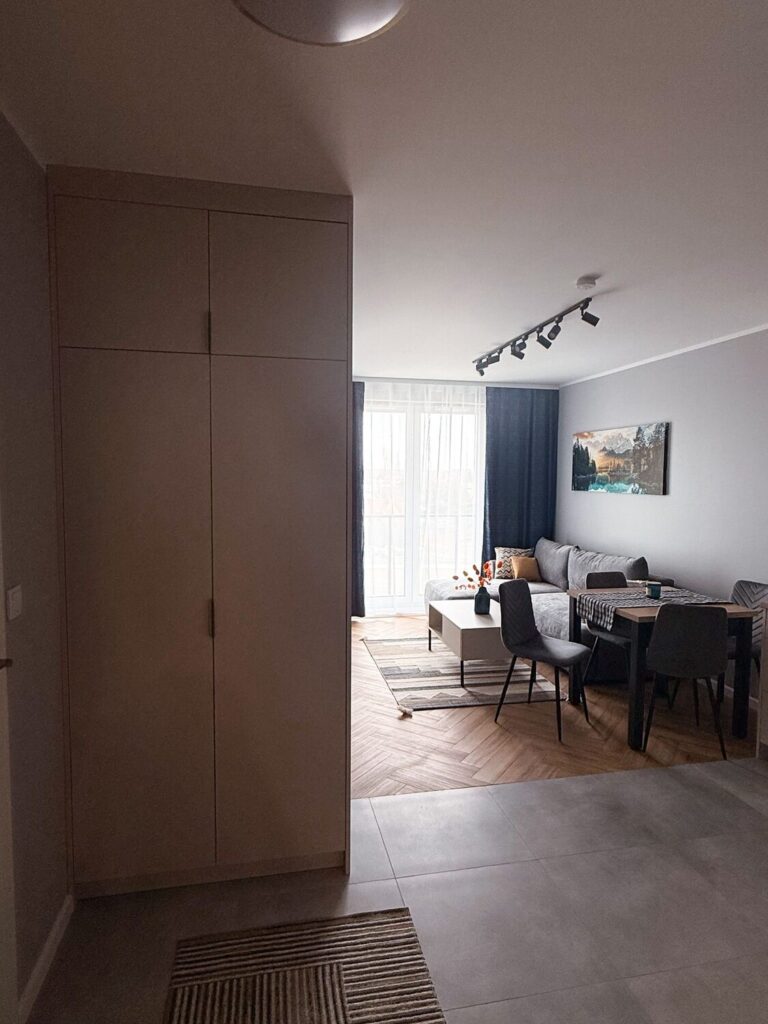 Przedpokój z jasną szafą i płytkami na podłodze, widok na salon, realizacja Remoart